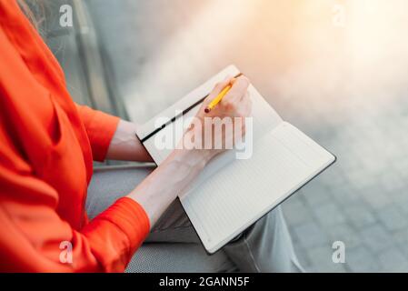 Caucasian girl sitting in the city and making notes in a notebook. Stock Photo