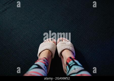 female feet with black pedicure in pink fluffy slippers on a dark semi-background, top view, copy space. Stock Photo