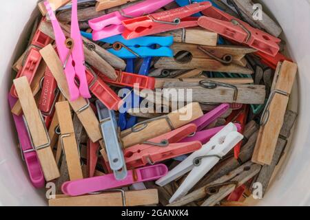 A white bucket of colored plastic and wooden clothes pegs Stock Photo