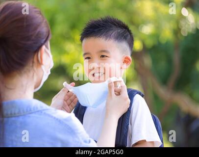 Happy Mother help son wearing medical mask at school Stock Photo