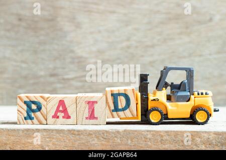 Toy forklift hold letter block d to complete word paid on wood background Stock Photo