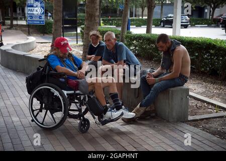 Tampa, Florida, USA. 31st July, 2021. Homeless men and women pass the time in the shade of trees along a downtown Tampa street. The town's few shelters are filled to capacity, advocates said. 'We get a lot of homeless people who comer here with a one-way bus ticket from other cities,'' a local police officer noted. 'Many of those who sleep on the streets have mental illness issues,'' he said. (Credit Image: © Robin Rayne/ZUMA Press Wire) Stock Photo