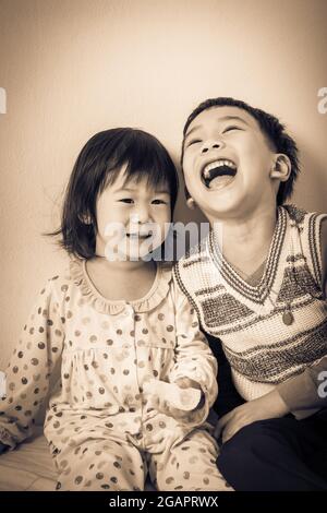 Little asian (thai) children happily, brother laughing and sister smiling, loving and bonding of sibling concept. Cream tone background. Vintage pictu Stock Photo