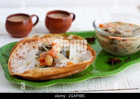 Appam, Hoppers and mutton stew Kerala breakfast food and Indian milk tea chai, christian breakfast India Sri Lanka Tamil Nadu fermented rice pan cake. Stock Photo