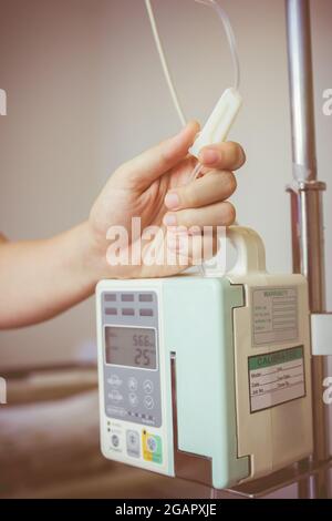 Nurse's hands regulation infusion pump intravenous (IV) drip in hospital room. Health care under medical observation. Vignette and vintage picture sty Stock Photo