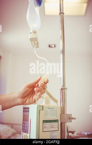 Nurse's hands regulation infusion pump intravenous (IV) drip in hospital room. Health care under medical observation. Vignette and vintage picture sty Stock Photo