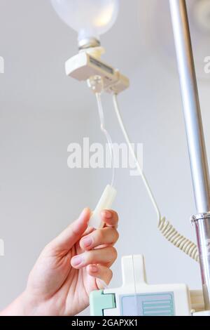 Nurse's hands regulation an intravenous (IV) drip in hospital room. Health care under medical observation. Stock Photo