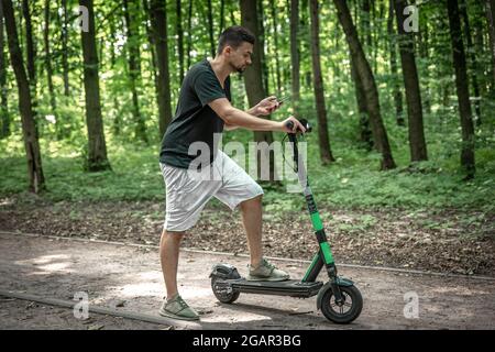 Young attractive man using his smartphone with an electric scooter. Stock Photo