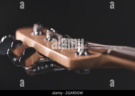 Detail of a tuning post on the wooden headstock of an electric bass guitar. Stock Photo