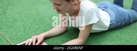 Smiling woman lies on agreen lawn with laptop Stock Photo