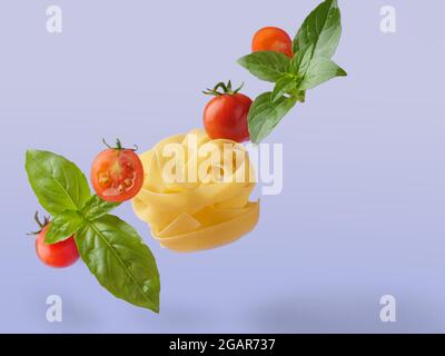 Flying in the air, raw fettuccine pasta with cherry tomatoes and basel leaves. Colored isolated. Stock Photo