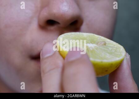Southeast Asian, Chinese and Myanmar young man with cold flu gets loss of smell called anosmia. He smells scent of lemon while staying at home. Closeu Stock Photo