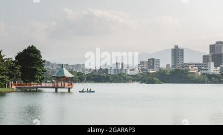 Fukuoka, Japan - A boat and a hexagonal, vermilion pavilion on a large pond at Ohori Park, or Ōhori-kōen, a pleasant city park in central Fukuoka. Stock Photo