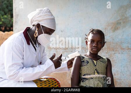 In this image, a tense little African schoolgirl is waiting for her pediatrician to inject a dose of vaccine into her arm Stock Photo