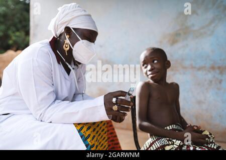 In this image, a sick tiny little african boy with a worried expression on his face is looking at the nurse who is preparing an injection for him Stock Photo