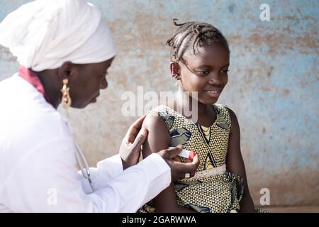 In this closeup, a gentle black nurse is measuring the axillary temperature of a smiling little African girl