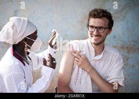 IN this image, a black nurse wearing a protective mask, with syringe and gauge in her hands is preparing to inject a booster dose of vaccine in the ar Stock Photo