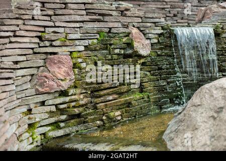 Artificial waterfall. Water runs over the stones. Landscaping in the park. Stock Photo