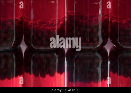 Four glass jars with home-preserved red cherries and their reflections Stock Photo