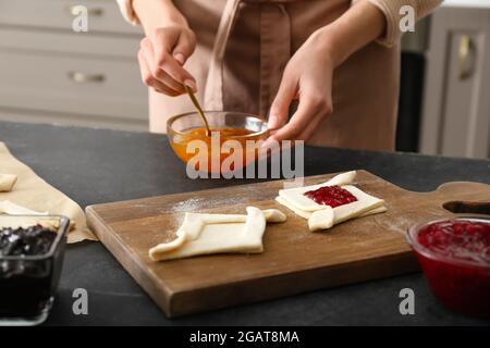 Woman filling Danish pastry with fruit jam on kitchen table Stock Photo