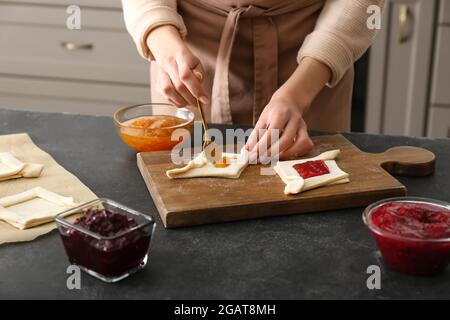 Woman filling Danish pastry with fruit jam on kitchen table Stock Photo