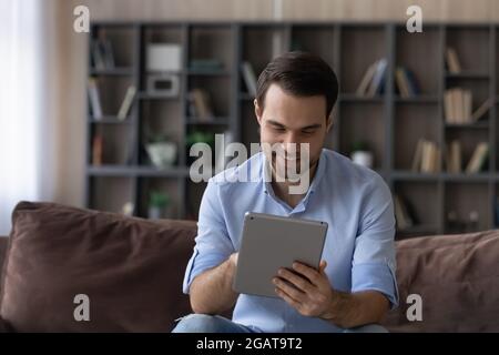 Focused millennial guy student enjoy using digital tablet at home Stock Photo
