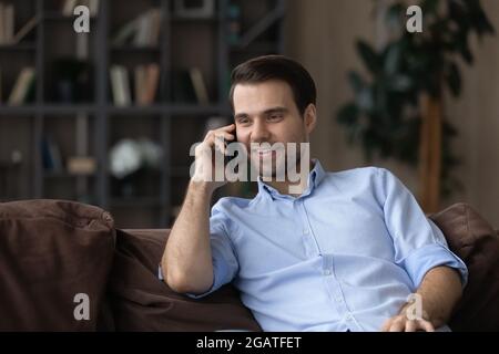 Smiling young man enjoy phone talk holding gadget at ear Stock Photo