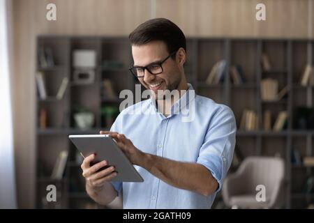 Smiling young man play on tablet pc at living room Stock Photo