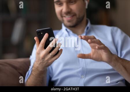 Happy young guy in wireless earphones using cellphone for videocall Stock Photo