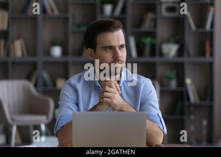 Millennial male entrepreneur sitting at desk thinking distracted from pc Stock Photo