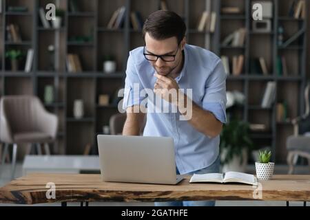 Focused young man stand by table look on laptop screen Stock Photo