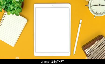 Top view of creative designer workspace with digital tablet mockup and office supplies on white desk, notepad, alarm clock and stylus pen, copy space Stock Photo