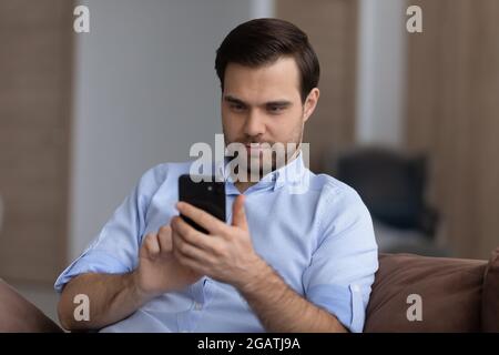 Focused guy spend time on couch browse web on phone Stock Photo