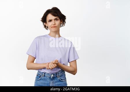 Skeptical young woman having doubts, look suspicious, squinting and flick an eyebrow unsure, standing in tshirt against white background Stock Photo