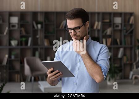 Concentrated millennial male engaged in reading book on digital tablet Stock Photo
