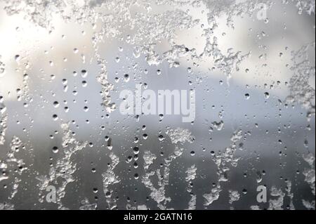 Snow, ice and droplets of rain partially thawing on a window pane in winter - background image for winter feature Stock Photo