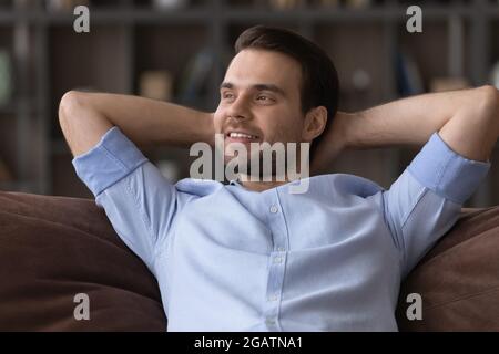 Calm young man lounge on sofa chill look aside dream Stock Photo