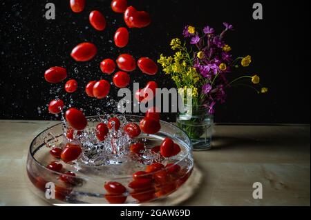 Fresh organic red baby plum tomatos (baby tomato,cherry tomato) group dropping on the water bowl with water splash copyspace Stock Photo