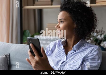 Smiling biracial woman use smartphone look in distance Stock Photo