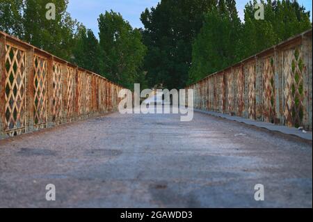 detail of a bridge with metal railing with a road and trees in the background Stock Photo