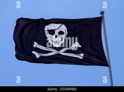 Pirate flag also known as a Jolly Roger flag or a Skull and Cross Bones Flag, pictured against a blue sky. Stock Photo