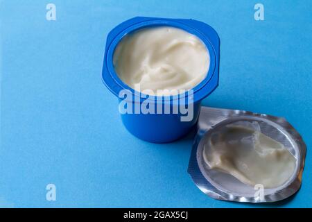 Yogurt cup with creamy yoghurt in blue pot and foil lid isolated on blue background with space for text Stock Photo
