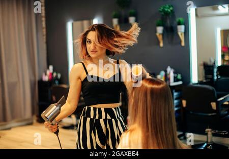 Happy woman with stylist making hairdo at salon. Competent female hairdresser deciding what to do in hair salon with brunette female client. Two beaut Stock Photo
