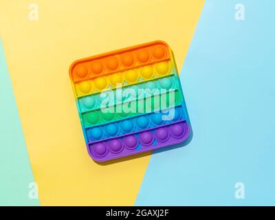 Popit on multicolor background with copy space. Popular silicone colorful antistress pop it toy for child on фягку, yellow and blue paper background. Top view from above. Simple dimple Stock Photo