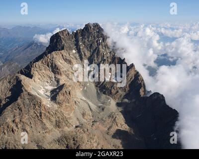 AERIAL VIEW. Southern craggy rock face of Monte Viso (3841m) with clouds to the east above the Po Plain. Province of Cuneo, Piedmont, Italy. Stock Photo