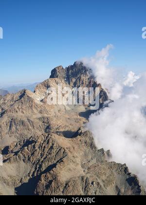 AERIAL VIEW. Southern craggy rock face of Monte Viso (3841m) with clouds to the east above the Po Plain. Province of Cuneo, Piedmont, Italy. Stock Photo