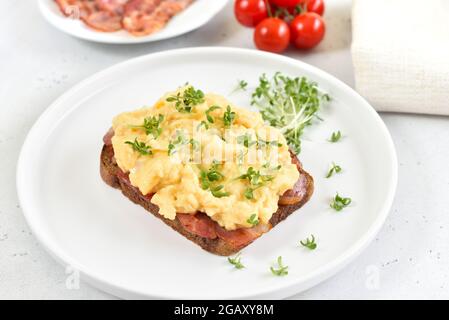 Scrambled eggs with microgreen and bacon on bread, close up Stock Photo