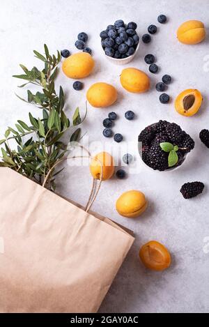 Ripe apricots, blueberries, blackberries scattered on a white background, purchase of summer berries, paper bag and apricots, blueberries, healthy foo Stock Photo