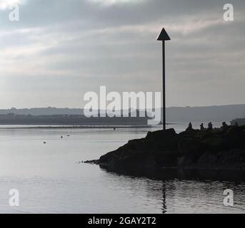 View Of People Sitting On A Breakwater and Groyne Warning Marker From Avon Beach Looking Over To the Black House And Mudeford Sandspit In Winter Chris Stock Photo