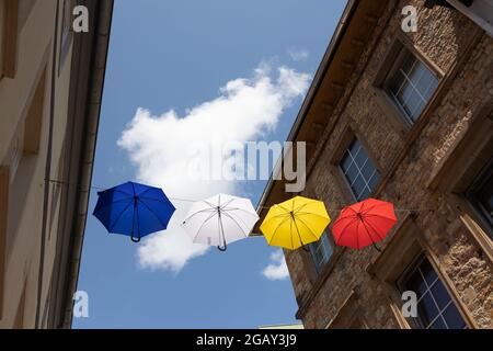 Colourful umbrellas hang on a rope between houses above the pedestrian zone of Bad Kreuznach, Rhineland-Palatinate, Germany. Stock Photo